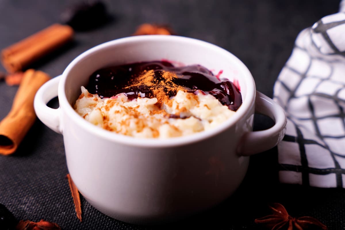 Postre en taza con arroz con leche, canela y salsa de frutas rojas, ideal entre los postres peruanos para vender.