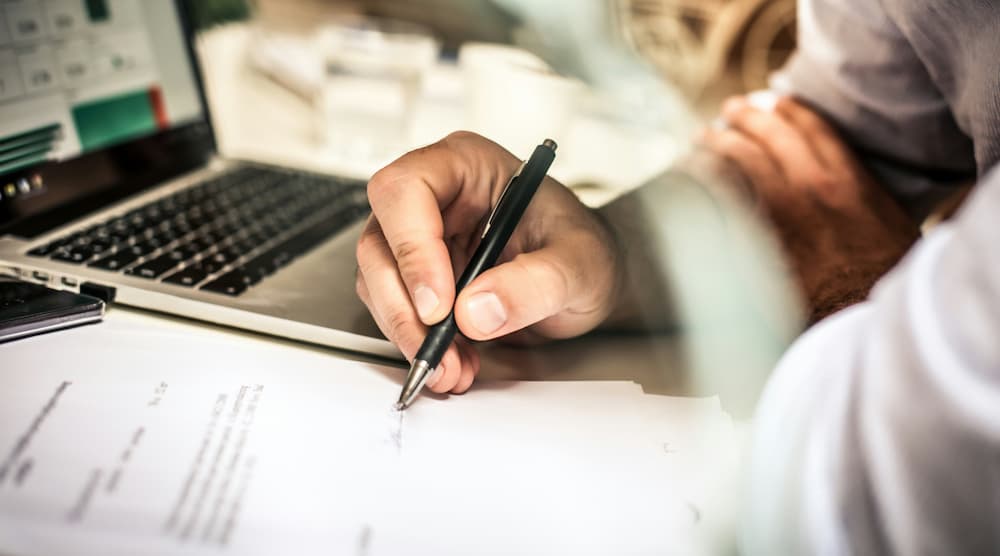 Persona escribiendo un plan de negocios mientras trabaja en un portátil.