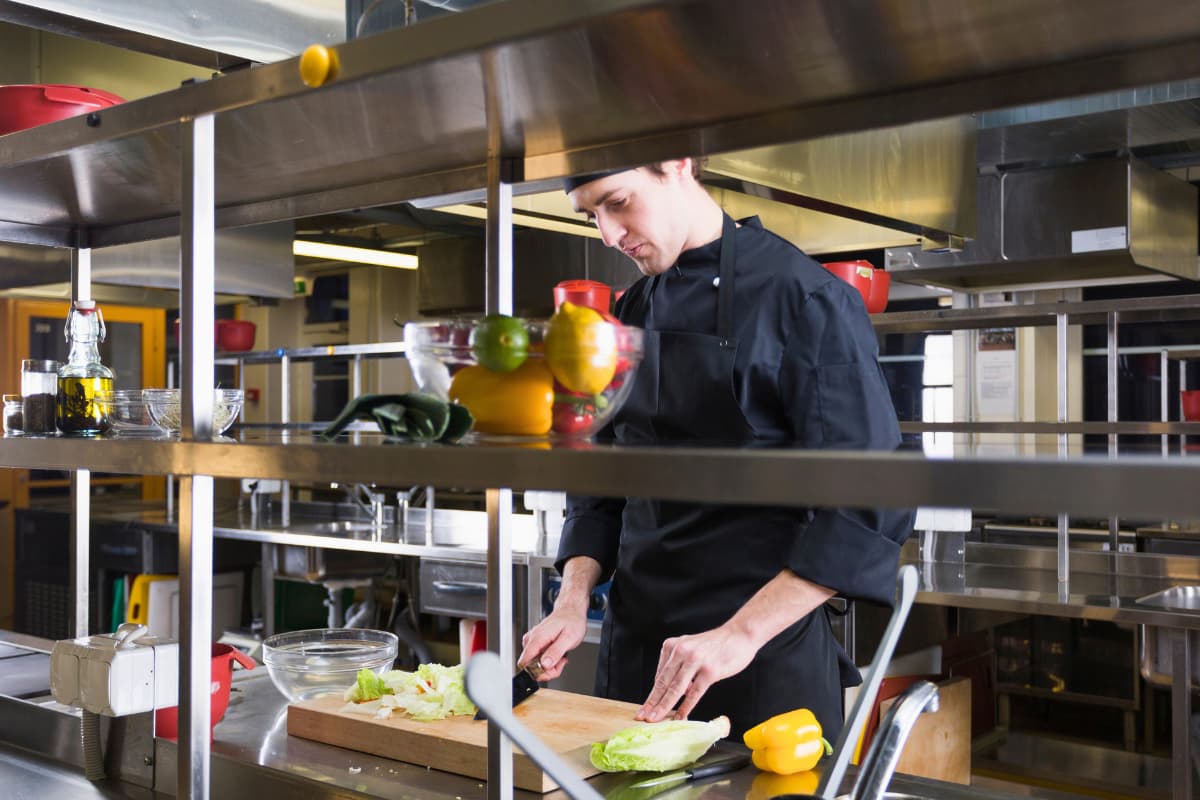 Hombre cortando vegetales en una cocina profesional, ideal para aprender cómo montar una cocina oculta con éxito.