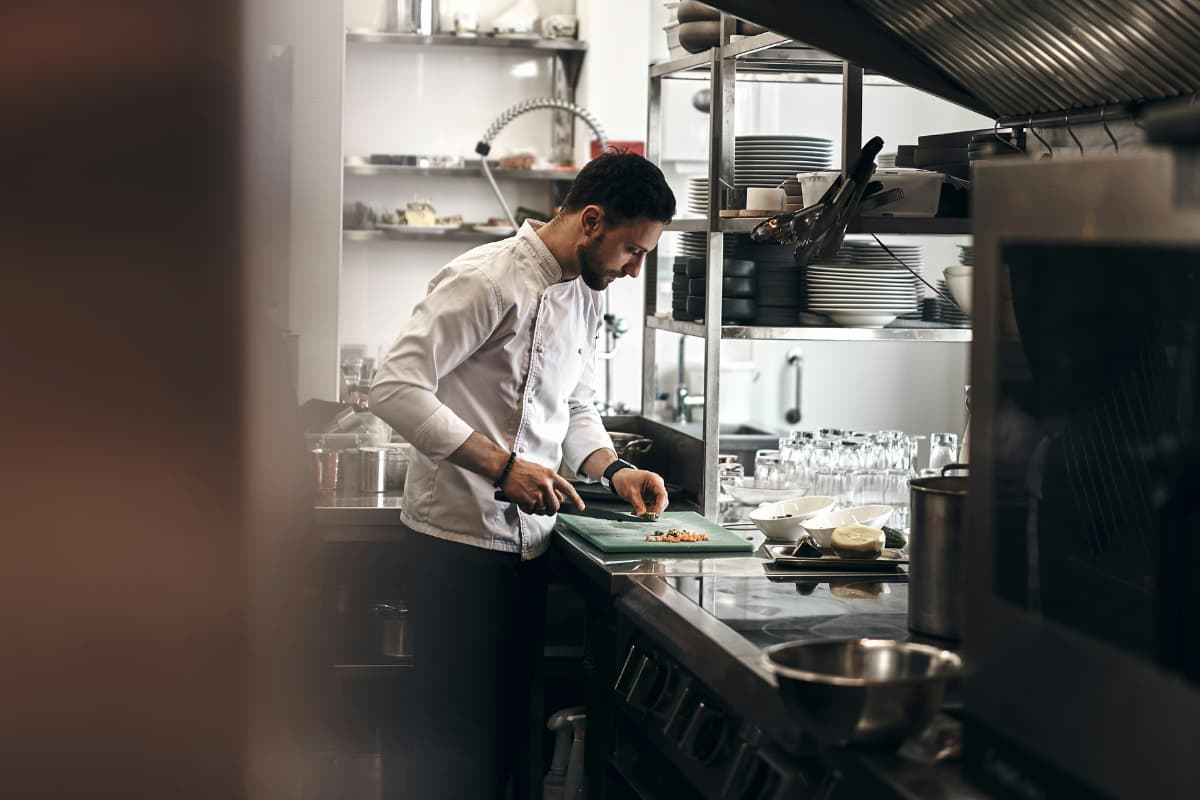 Chef em uma cozinha profissional usando equipamentos de cozinha industrial, cortando ingredientes em um ambiente organizado e moderno.