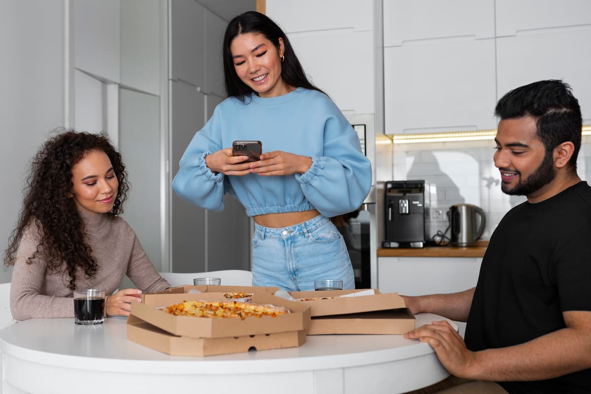 Três amigos em volta de uma mesa com pizzas, enquanto uma pessoa tira foto da comida, ilustrando recuperação de vendas por engajamento