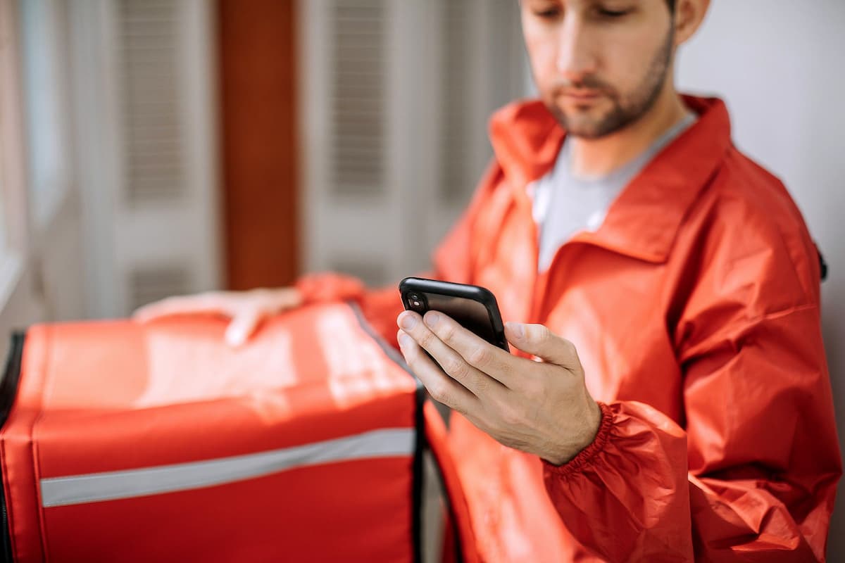 Entregador com mochila térmica e celular, simbolizando estratégias de como vender mais no delivery com foco em tecnologia.