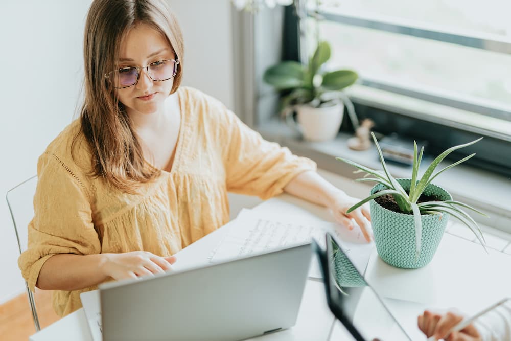 Gerente de resturante concentrada trabalhando em um laptop em um ambiente iluminado, cercada por plantas