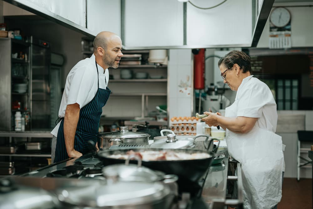 Dos chefs trabajando en una dark kitchen, preparando ingredientes y cocinando en un entorno profesional con equipos de cocina industrial