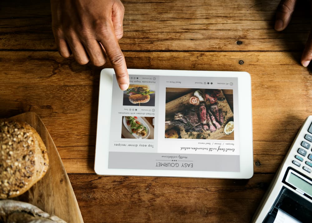 Uma mão interagindo com um tablet que exibe cardápio de restaurante