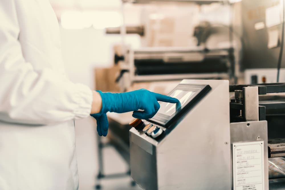 Trabajador con guantes azules operando una máquina en una cocina oculta