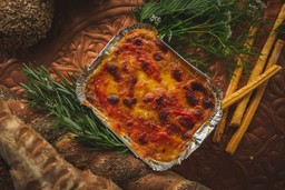 Lasanha recém-assada em embalagem para viagem cercada por pães e ervas frescas, ideal para dicas sobre como montar um delivery de massas.