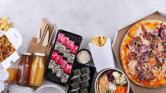 A imagem apresenta uma vista superior (flat lay) de uma mesa com diversos pratos de comida delivery organizados lado a lado sobre um fundo claro e neutro.