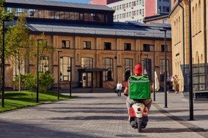 Repartidor en moto con mochila verde circula por zona urbana, reflejando los tiempos de entrega en dark kitchen eficientes.