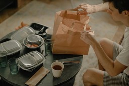 Homem abrindo sacolas de comida em casa após receber uma entrega, destacando a conveniência de um programa de fidelidade para delivery.