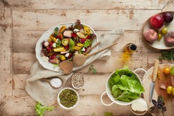 Uma mesa de madeira rústica repleta de ingredientes frescos e naturais, incluindo uma salada colorida com folhas verdes, tomates cereja amarelos e vermelhos, fatias de pêssego e pedaços de queijo em um prato branco.