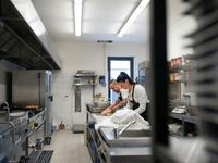 A imagem mostra o interior de uma cozinha profissional, que pode ser identificada como uma dark kitchen (ou cozinha fantasma), um modelo de negócio voltado exclusivamente para entregas.