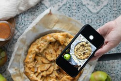 Uma mão segurando um celular tirando foto de uma torta de maçã caseira