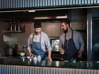 Essa imagem mostra dois chefs ou cozinheiros profissionais trabalhando juntos em um ambiente moderno e bem equipado, que se assemelha bastante ao modelo de uma dark kitchen.
