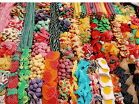 La imagen muestra una colorida y abundante variedad de golosinas dispuestas de manera ordenada. Hay gomitas de muchas formas y sabores: ositos, corazones, huevos fritos, delfines, serpientes, estrellas, fresas, pizzas en miniatura, entre otras figuras divertidas.