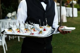 Garçom segurando bandeja com aperitivos sofisticados, ideal para ilustrar como iniciar um serviço de catering.