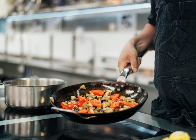 Delivery de comida: Hombre cocinando en una cocina industrial, en una sartén con comida dentro