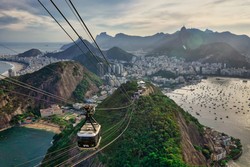 Bondinho do Pão de Açúcar suspenso, com vista para a cidade do Rio de Janeiro ao fundo. A imagem destaca a beleza natural e urbana do local, incluindo praias, montanhas e a Baía de Guanabara.