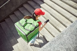 Entregadora usando mochila verde descendo escadas com celular na mão