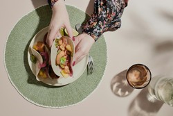 Plato con tacos deliciosos siendo sostenidos por manos femeninas, en una mesa cuidadosamente puesta con un mantel verde y copas de bebida