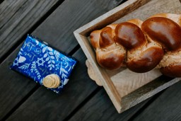 Pão challah, da culinária kosher, trançado em bandeja de madeira ao lado de tecido azul com moeda.