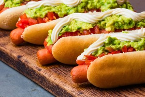 Completos chilenos en fila sobre tabla de madera, con palta, tomate y mayonesa — tipos de completos chilenos clásicos.