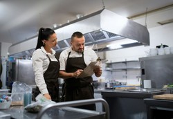 Dois chefs em uma cozinha profissional revisando manual e anotando instruções
