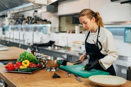 Uma chef prepara vegetais frescos em uma cozinha profissional, exemplificando as operações no setor de food service.