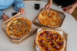 Imagem de três sabores de pizza populares, incluindo calabresa, frango com catupiry e vegetariana, em caixas de delivery.