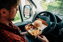 Motorista comendo fast food no carro, representando tendências gastronômicas para 2025, como refeições práticas e convenientes.