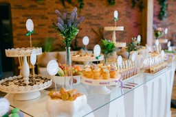 Mesa de catering elegante com diversos doces e um arranjo floral no centro, em um local sofisticado.