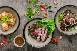 Três tigelas de comfort food deliciosas com carnes e vegetais frescos em uma mesa de madeira rústica.