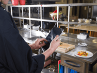 La imagen muestra a una persona vestida con un uniforme de chef negro, de pie en lo que parece ser una cocina profesional o industrial. 