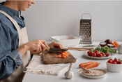 cocina sostenible: un joven cortando zanahorias en su mesa hay verduras, zanahorias, tomates y ajo, están cortando zanahorias en una tabla de cortar, está vestido con un delantal blanco