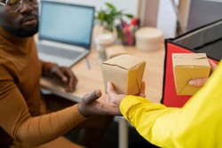 Entregador passando uma embalagem de comida para um cliente em um ambiente de trabalho