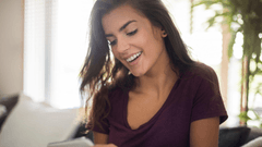 A imagem mostra uma mulher jovem sorrindo enquanto olha para o seu smartphone.