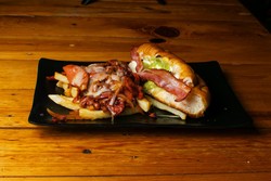 Um prato retangular preto sobre uma mesa de madeira apresenta uma refeição saborosa: batatas fritas carregadas com queijo derretido, bacon e possivelmente um molho de carne, ao lado de um sanduíche macio recheado com alface, bacon e outros ingredientes.