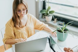 Gerente de resturante concentrada trabalhando em um laptop em um ambiente iluminado, cercada por plantas