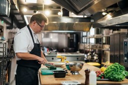 Chef preparando ingredientes em cozinha industrial, ilustrando práticas eficientes de como fazer um restaurante se expandir.