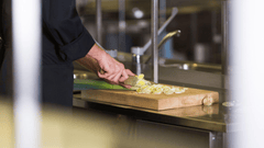 Esta  imagem foca no trabalho de precisão e na técnica de um profissional de culinária em uma cozinha industrial.