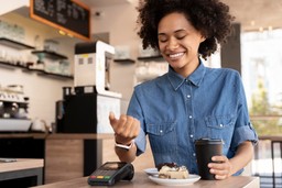 Cliente sorrindo enquanto paga com smartwatch, mostrando formas de pagamento modernas e convenientes em um café.