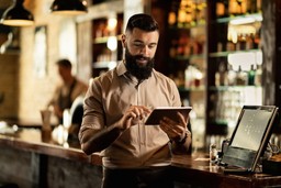 Homem usando tablet em restaurante, representando gestão da margem de lucro de um restaurante de forma eficiente.