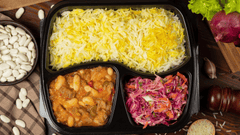 Uma marmita dividida em três compartimentos: arroz branco com açafrão na parte maior, feijão branco com carne em molho na lateral e uma salada colorida com repolho roxo e cenoura.