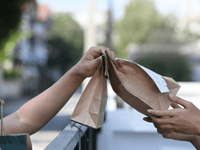 La imagen captura el momento de una entrega, mostrando manos interactuando con bolsas de papel.
