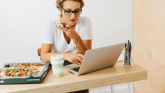 Esta imagem foca em uma mulher jovem e focada em sua tarefa, trabalhando em seu laptop enquanto desfruta de um lanche.