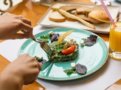 Prato delicioso com omelete de espinafre, decorado com tomate e ervas, acompanhado de pães e suco de laranja