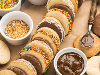 La imagen es una toma cenital, o plano picado, que muestra una exhibición apetitosa de alfajores y sus ingredientes de decoración, probablemente en una pastelería o para una sesión de fotos de alimentos.