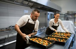 Dos chefs de cocina están organizando platos de verduras frescas y saludables en una cocina moderna.