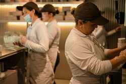 Funcionários de um restaurante trabalhando na cozinha, organizando alimentos e utilizando equipamentos em um ambiente limpo