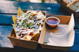 Uma caixa de nachos sobre uma mesa de madeira, com chips crocantes e queijo derretido visíveis.